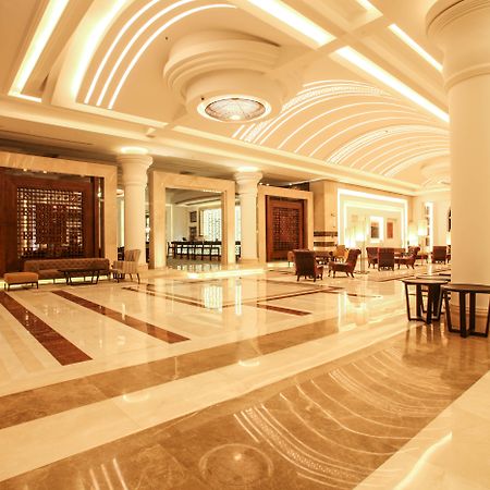 Savoy Le Grand Hotel Marrakech Marakeş Dış mekan fotoğraf The photo shows an elegant hotel lobby with a spacious and luxurious design. The floor features a mix of light and dark marble patterns, creating an appealing visual contrast. The ceiling has a modern, curved design with soft lighting that enhances t