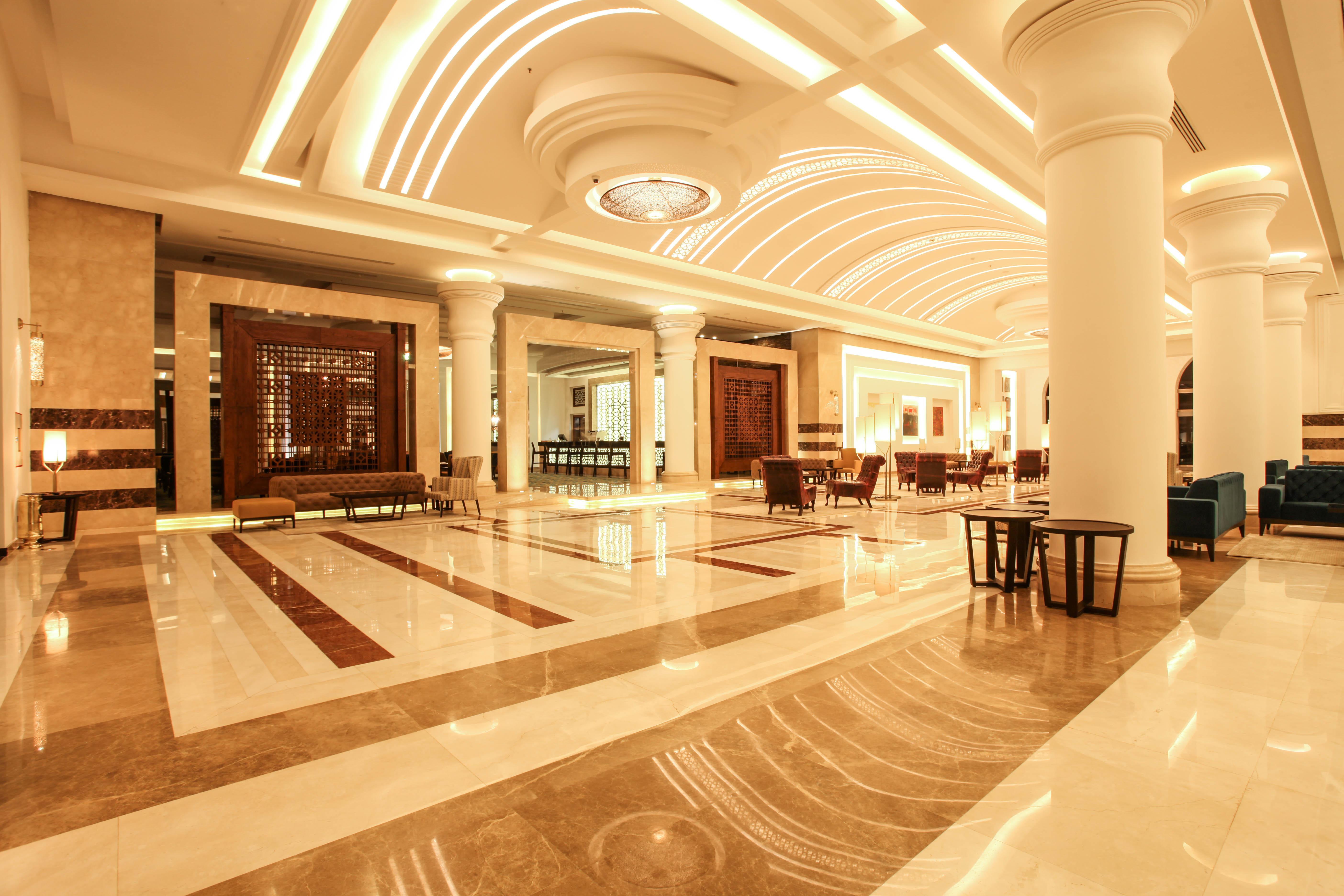 Savoy Le Grand Hotel Marrakech Marakeş Dış mekan fotoğraf The photo shows an elegant hotel lobby with a spacious and luxurious design. The floor features a mix of light and dark marble patterns, creating an appealing visual contrast. The ceiling has a modern, curved design with soft lighting that enhances t