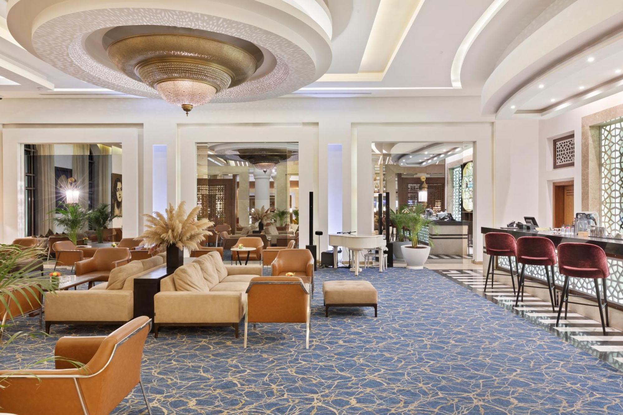 Savoy Le Grand Hotel Marrakech Marakeş Dış mekan fotoğraf The photo shows a stylish and elegantly designed lobby or lounge area. It features comfortable seating, including light-colored sofas and armchairs, arranged in a welcoming manner. The space has a luxurious feel, with a decorative ceiling, a large ch